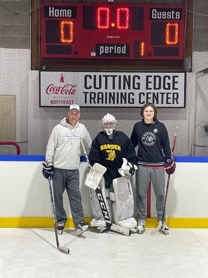 Two coaches and a goalie on the ice under the Cutting Edge Training Center scoreboard