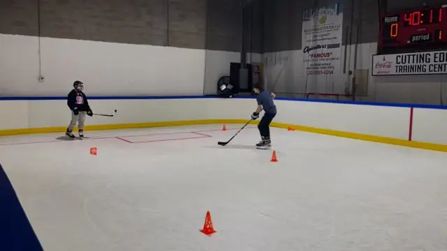 Two young players skating a puck drill around cones